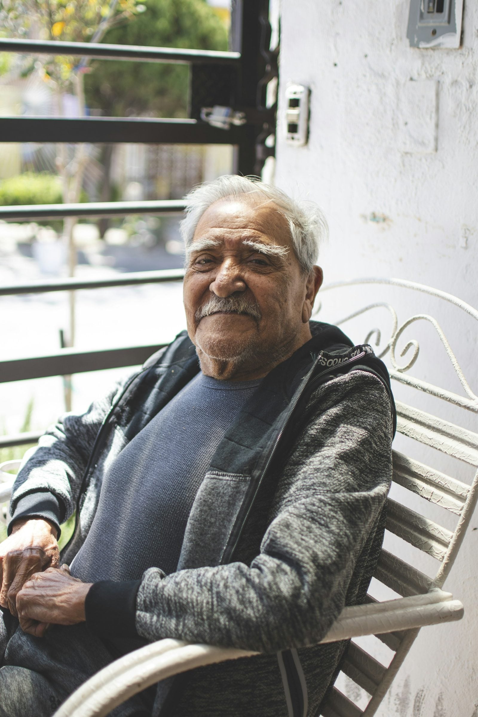 An older man sitting on a chair on his balcony in the morning light