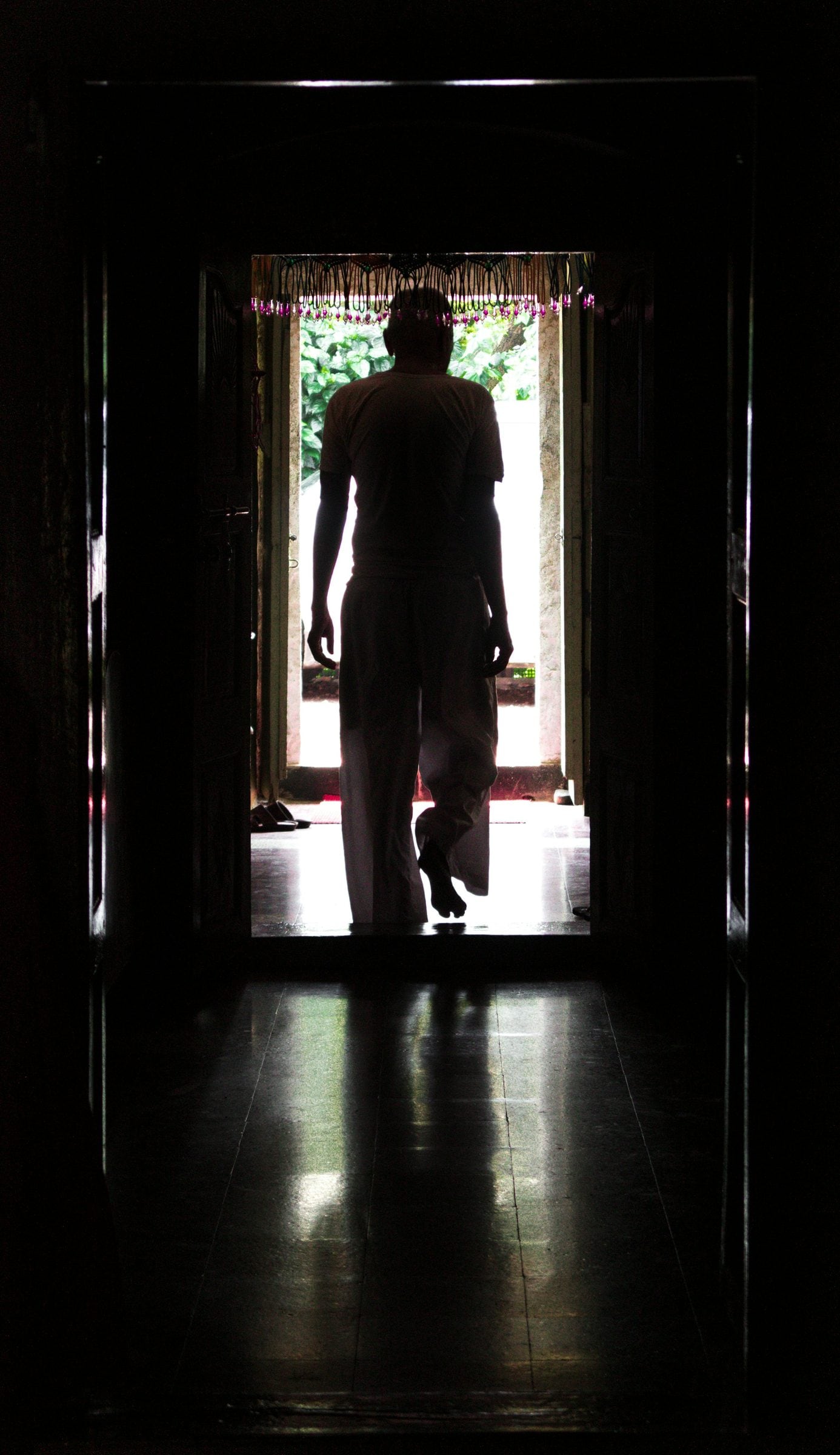 A silhouette standing in a bright doorway at the end of a dark hall
